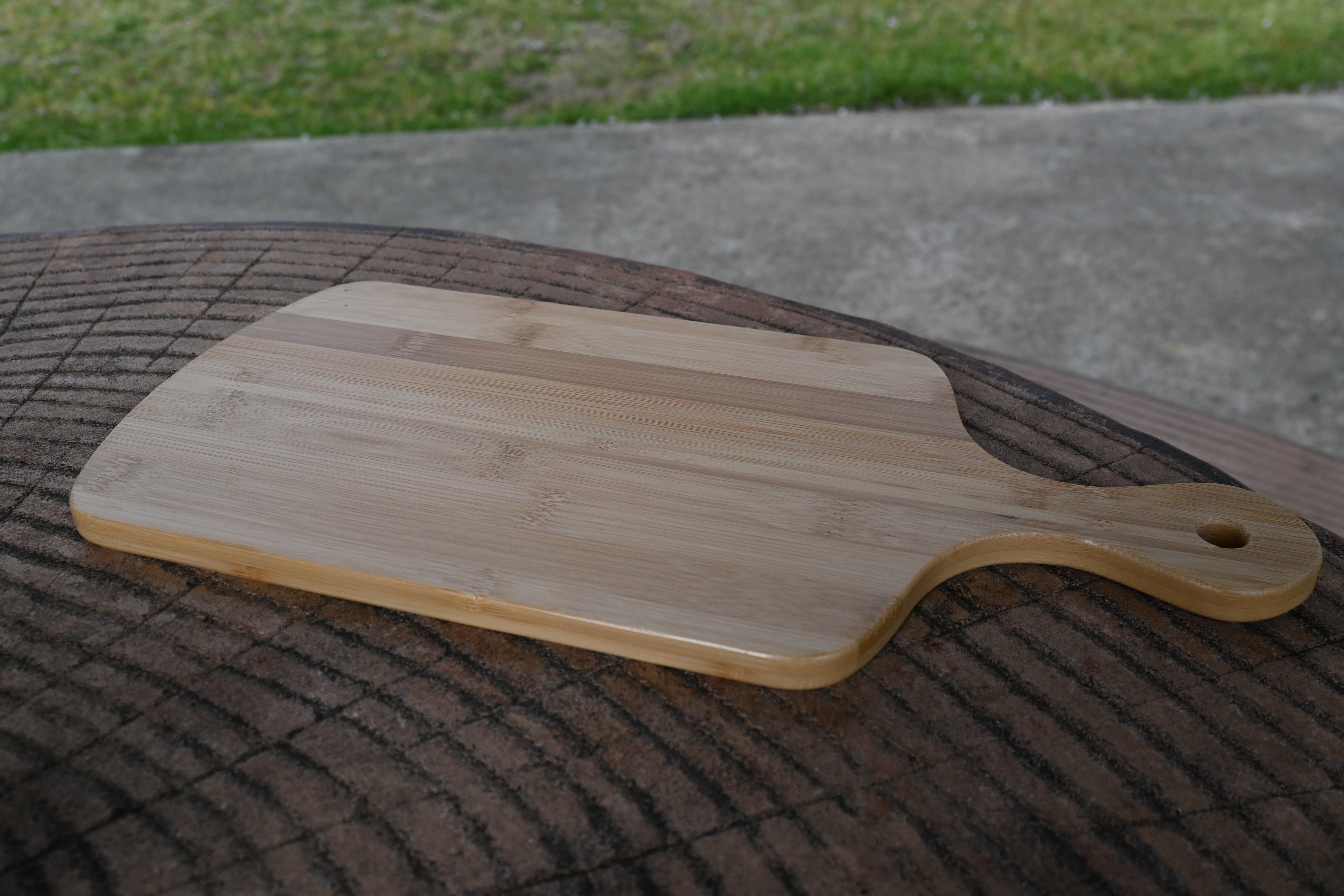 丸太の卓上に置かれた、取手付きの竹製カッティングボードを斜めから捉えた写真