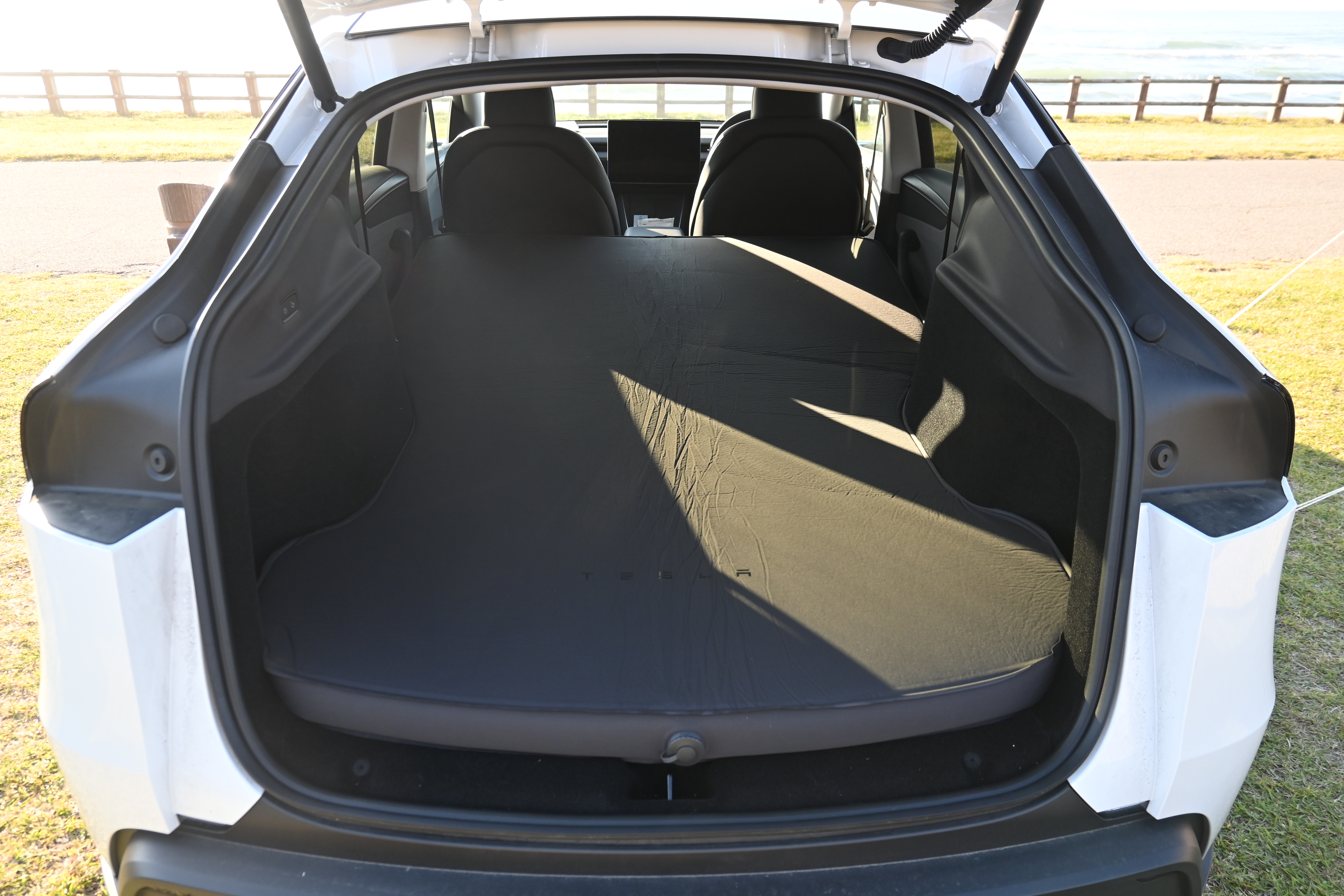 Model Y のリアハッチを開け、後部座席を倒した上に純正エアーマットレスを展開した状態を後方から撮影した夕方の写真